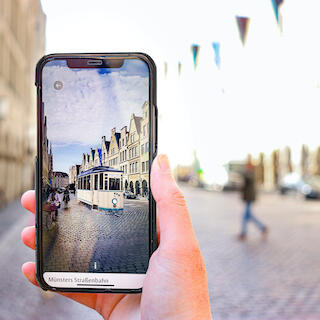 Ein Handydisplay, der den Prinzipalmarkt Münster durch die EXPLORE App zeigt